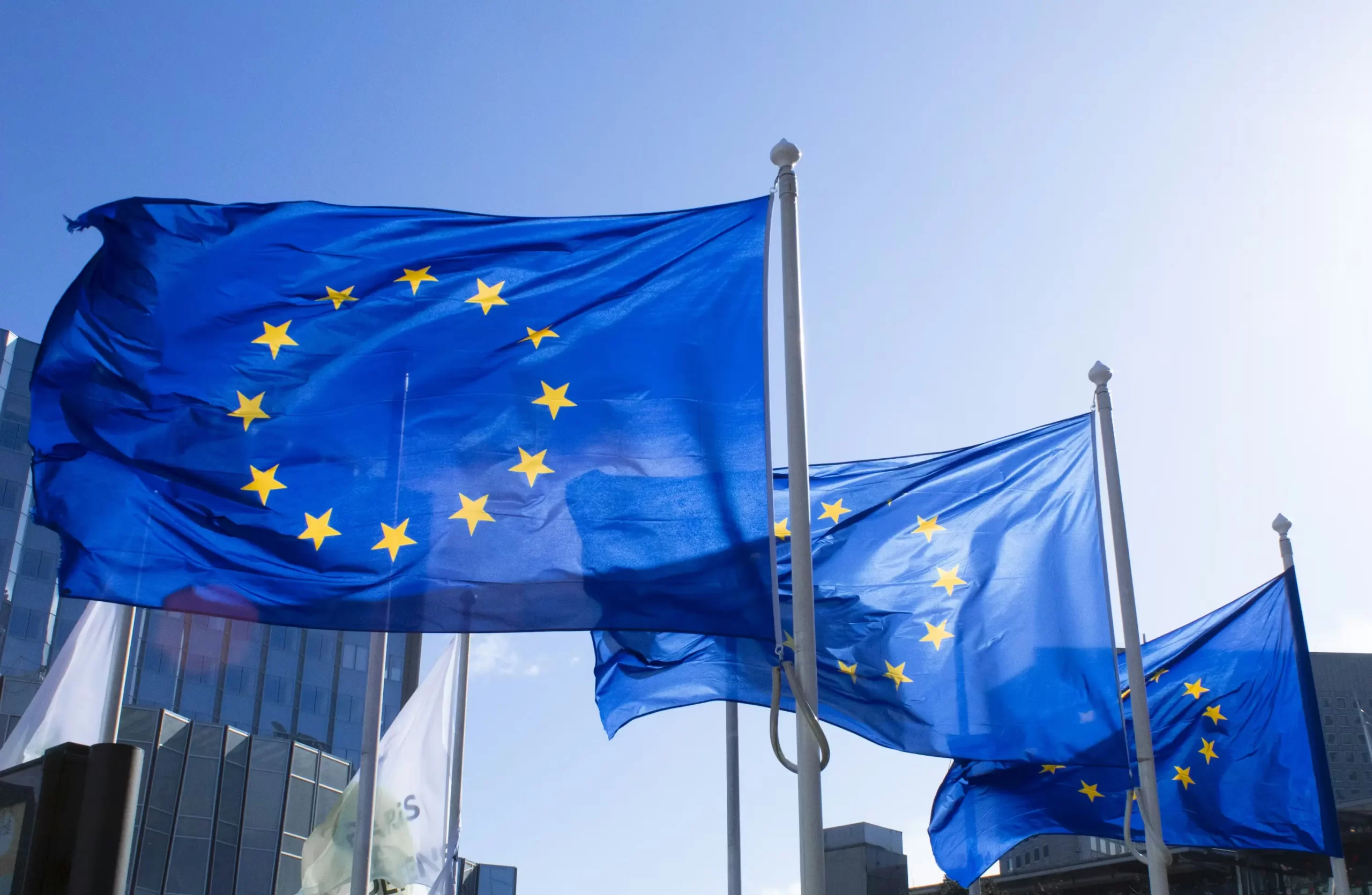 Waving European Union flags against a clear blue sky.